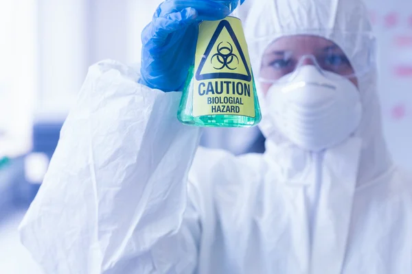 Scientist in protective suit with hazardous chemical in flask