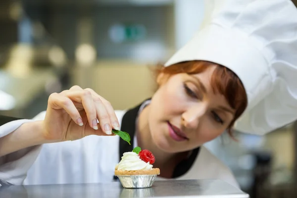 Focused head chef putting mint leaf on little cake