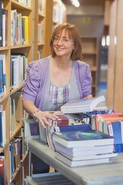 Female mature librarian returning books in library