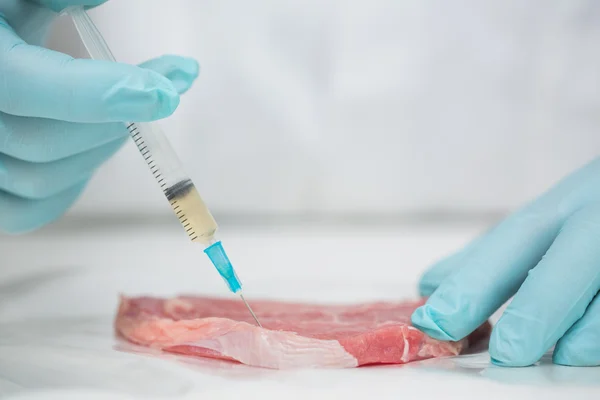 Close-up of gloved researcher's hands injecting meat