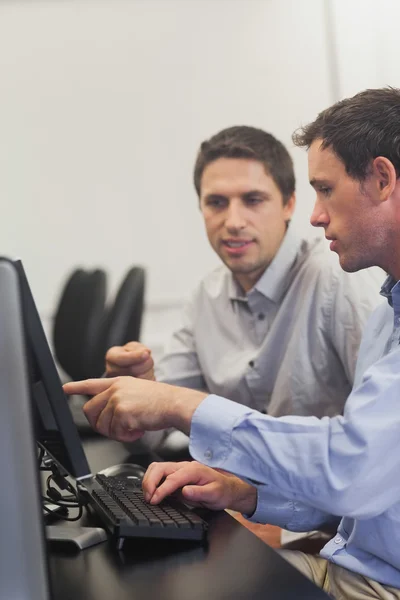 Two mature men talking while sitting in front of computer