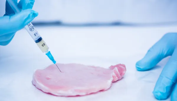 Close-up of gloved researcher's hands injecting meat