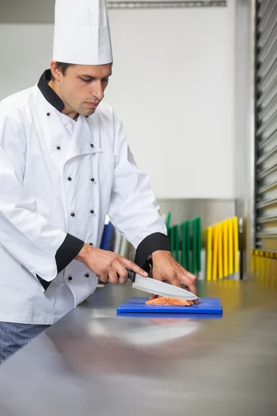 Serious chef cutting raw salmon with knife on blue cutting board