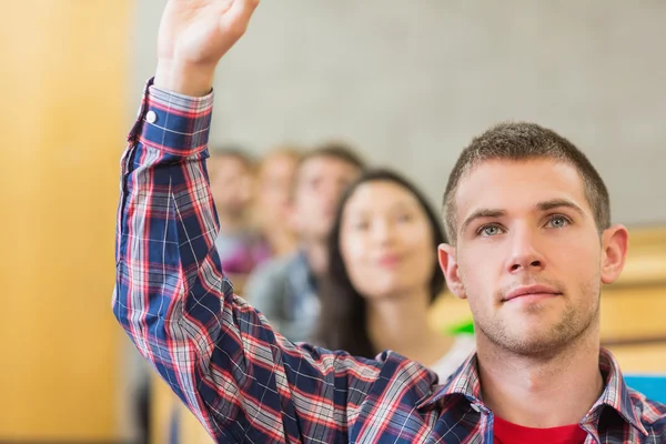 Close-up of a male student raising hand by others in classroom