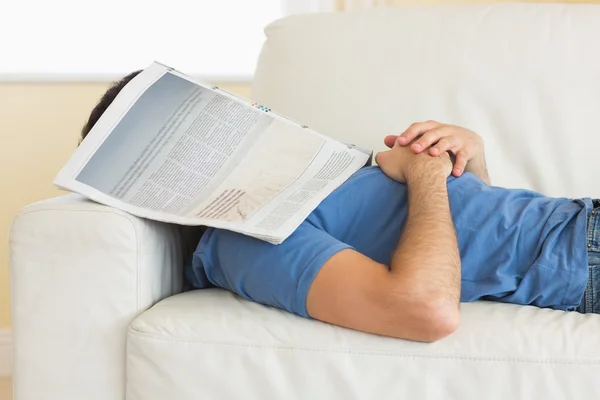 Casual man lying on couch with newspaper covering head