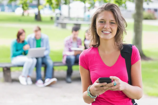 College girl text messaging with blurred students in park