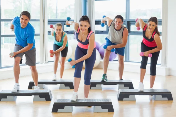 Instructor with fitness class performing step aerobics exercise with dumbbells