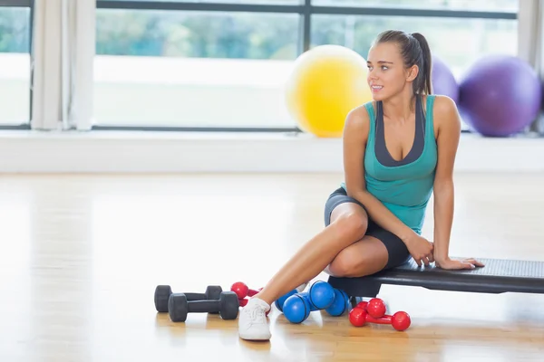 Young woman sitting with dumbbells in fitness studio