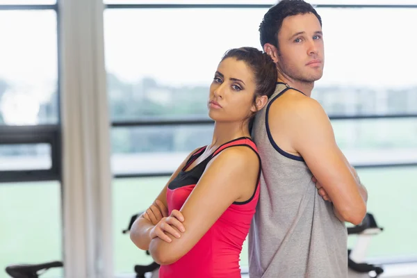 Serious young woman and man standing back to back in gym