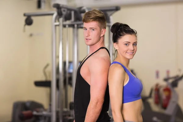 Sporty woman and man standing back to back in gym