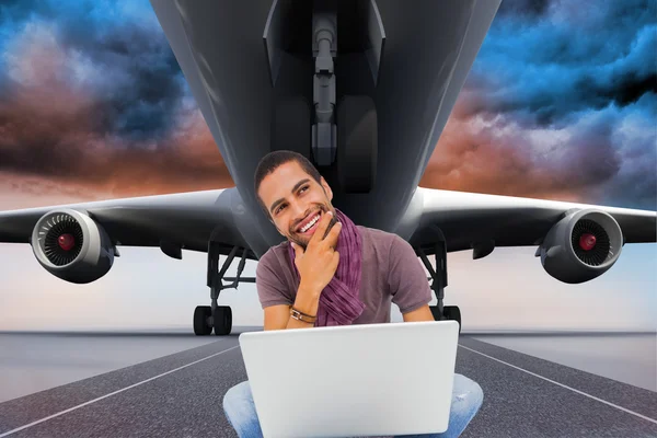 Thinking man sitting on floor using laptop and smiling