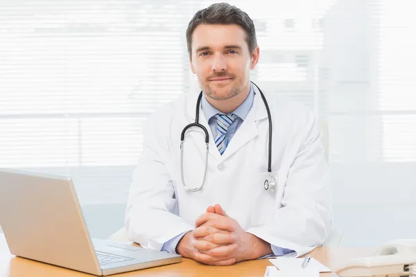 Male doctor with laptop at desk in medical office