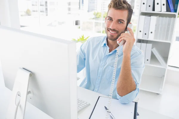 Smiling man using phone and computer in office