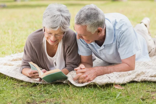 Relaxed senior couple reading book while lying in park