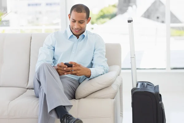 Man sitting on sofa sending a text waiting to depart on business