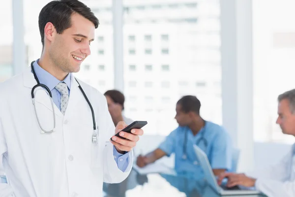 Doctor text messaging with group around table in hospital