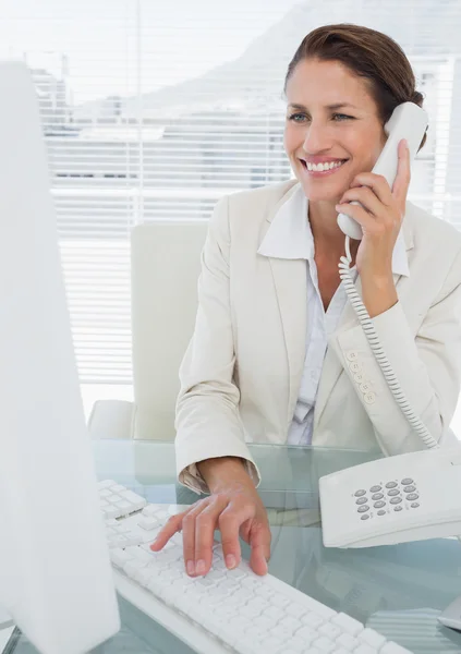 Smiling businesswoman using computer and phone