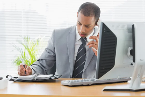 Businessman using computer and phone at office desk