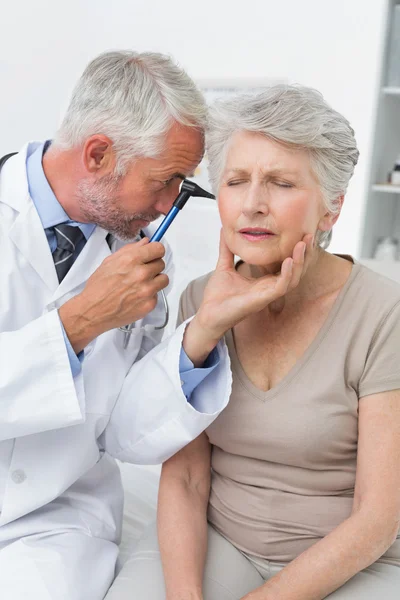 Male doctor examining senior patient\'s ear