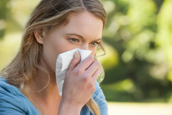 Woman blowing nose with tissue paper at park