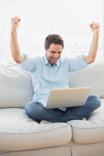 Cheering man using laptop sitting on sofa