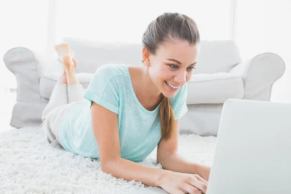 Happy woman lying on rug using her laptop