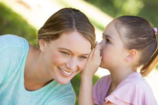Girl whispering secret into mother's ear at park