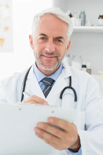 Smiling male doctor writing reports in medical office