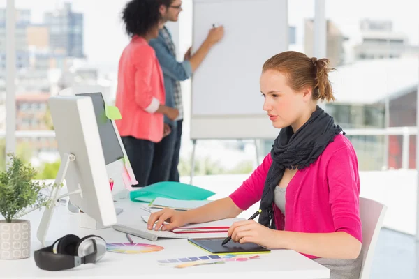 Female artist using graphic tablet with colleagues at office