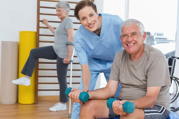 Therapist assisting senior man with dumbbells