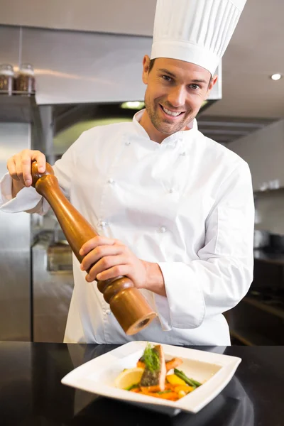 Smiling male cook grinding pepper on food in kitchen