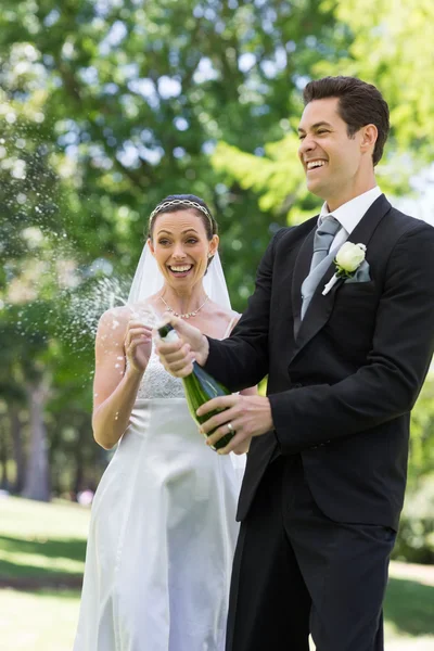 Newlywed couple popping cork of champagne