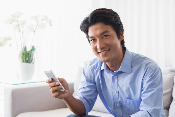 Happy man sitting on couch texting on phone