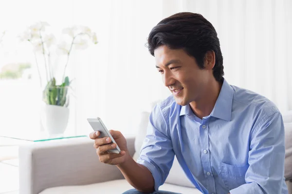 Happy man sitting on couch texting on phone