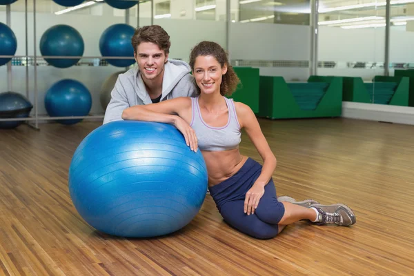 Woman leaning on exercise ball with trainer