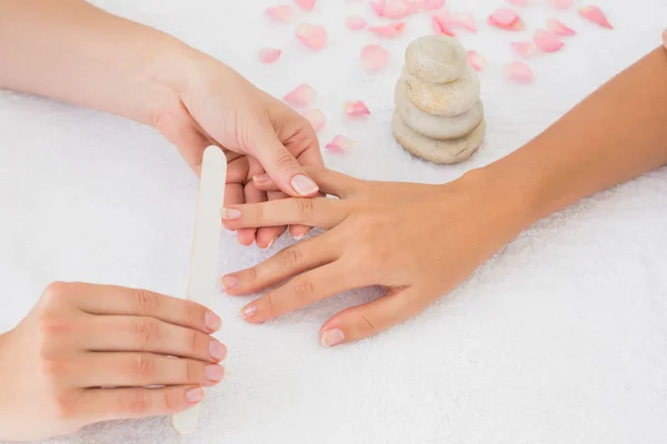 Beautician filing female client's nails at spa beauty salon