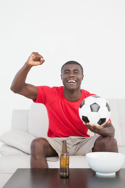 Football fan sitting on couch with ball cheering