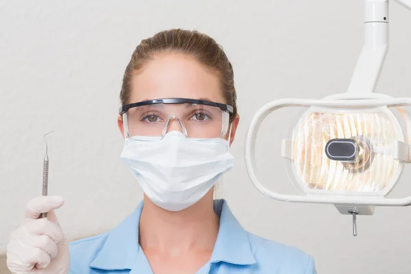 Dental assistant in mask holding dental explorer