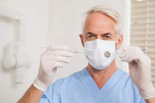 Dentist in surgical mask looking at camera holding tools