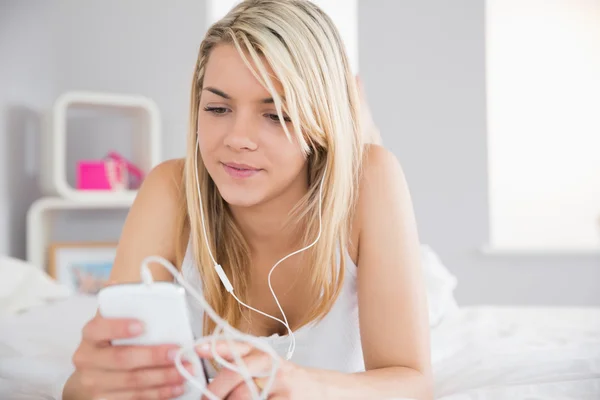 Relaxed woman listening music with mobile phone in bed