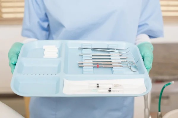 Dentist in blue scrubs holding tray of tools