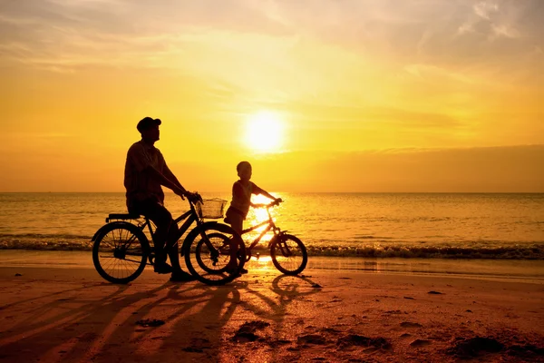 Father and son cycle ride on the beach in the sun rise