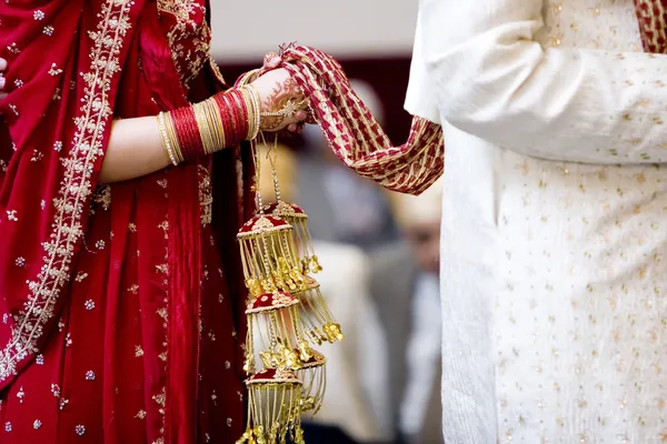 Hindu bride walks behind husband holding garb