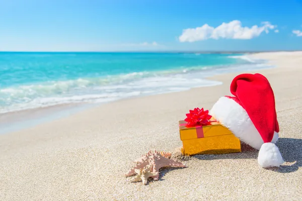 Santa Claus hat and christmas gift box on the seashore with sea