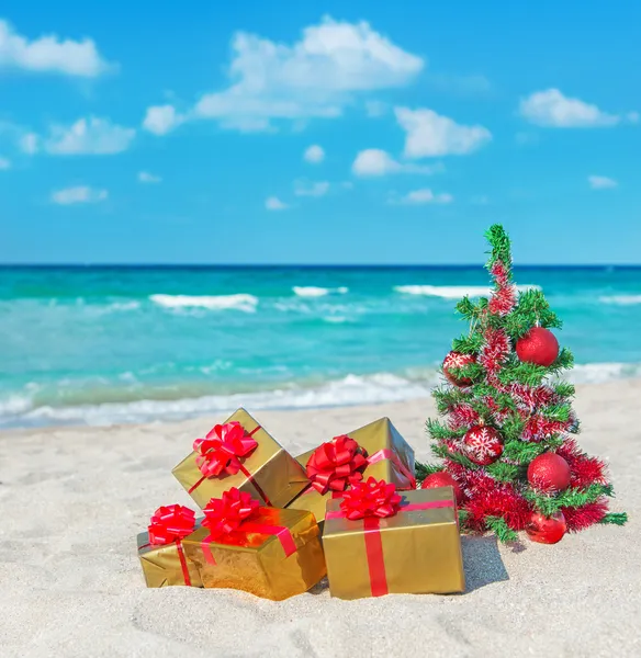 Christmas tree and golden gift with big red bow on the sea beach