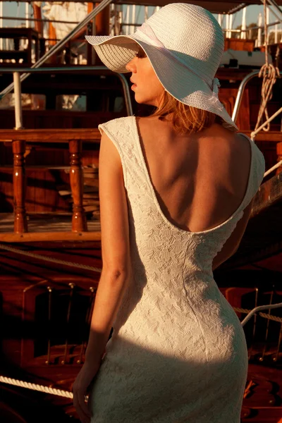 Back side view of lady with a hat and lace dress near the wooden yachts