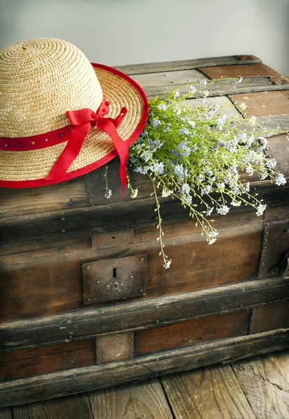 Blue summer flowers and straw hat on old vintage chest