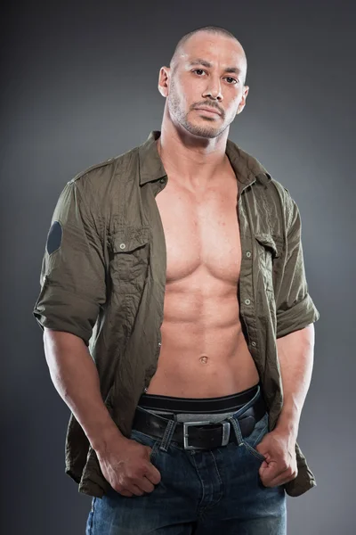 Muscled tough guy wearing green army shirt. Good looking man. Isolated on grey background. Studio shot. Healthy. Fitness.