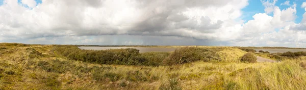 Panoramic shot of dutch dune landscape with lakes and stormy blue cloudy sky.