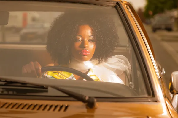 Retro 70s fashion african american woman driving in gold seventi